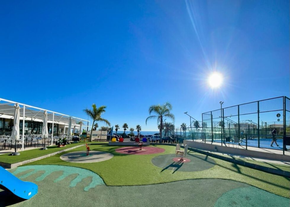 Parque infantil con palmeras y el mar al fondo