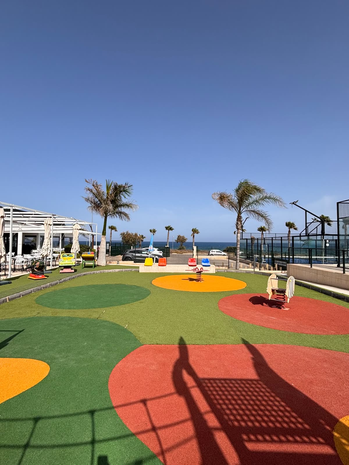 Parque infantil con palmeras y el mar al fondo